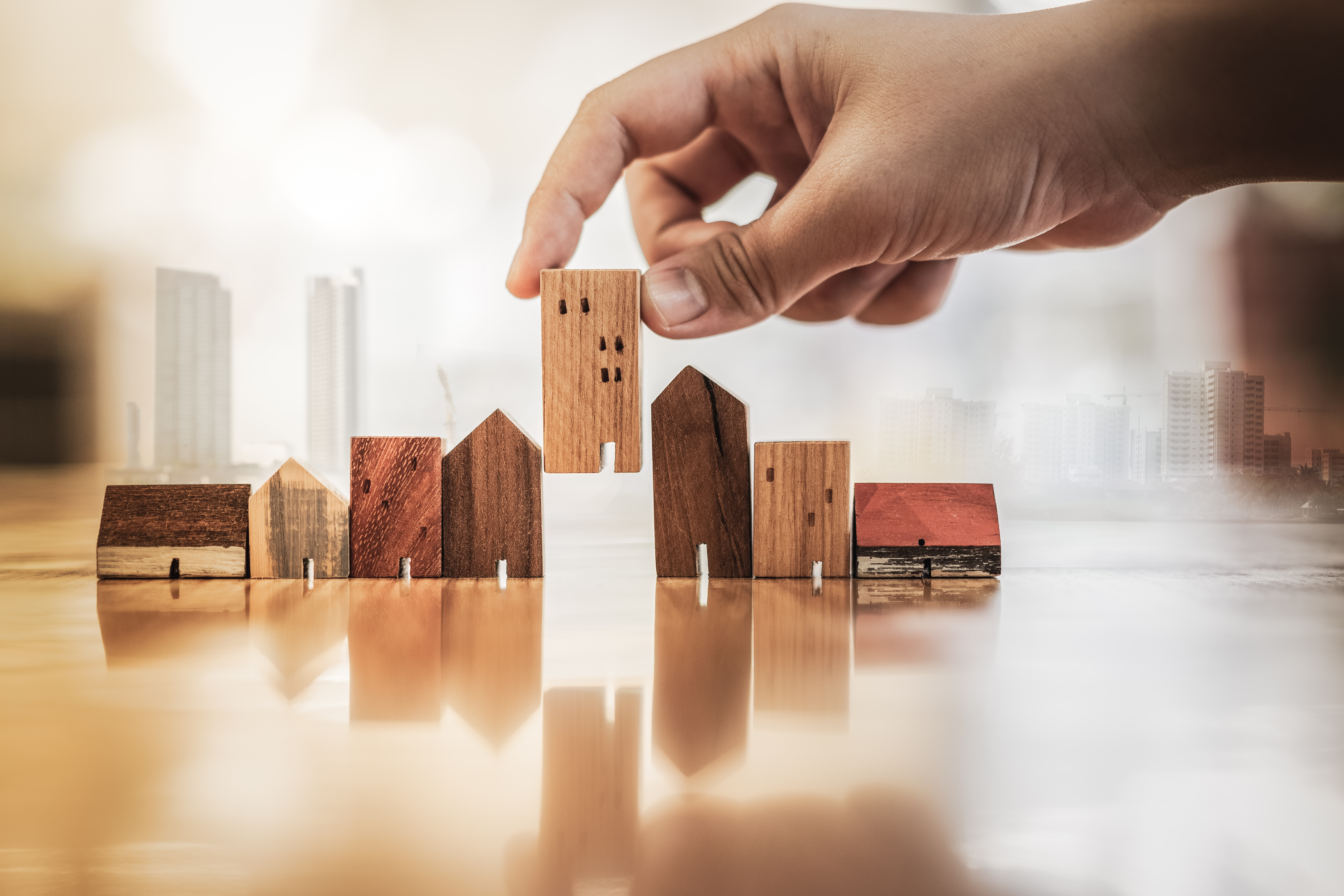 hand-choosing-mini-wood-house-model-from-model-on-wood-table-1